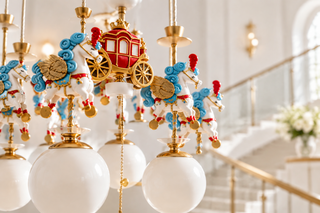 Carousel unicorn chandelier with a central red carriage, gold accents, and white frosted glass globe pendant lights.